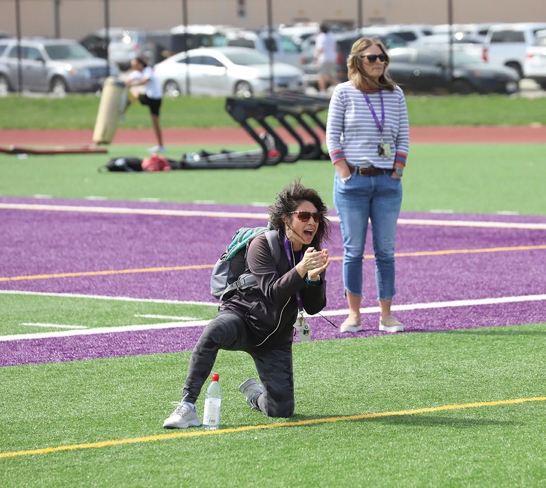 GISH Unified Track Coach, Andrea Hill, cheering on competitors while kneeling on the turf.